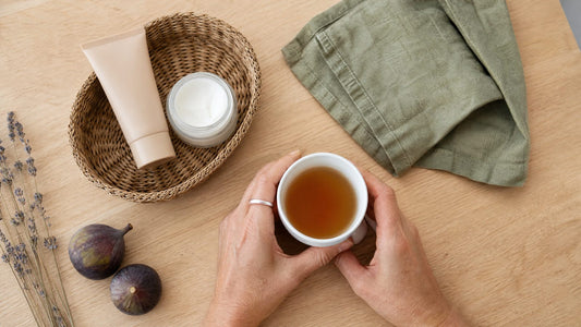 Mains de femme autour d'une tasse de thé, avec un tube de crème teintée sur une table claire